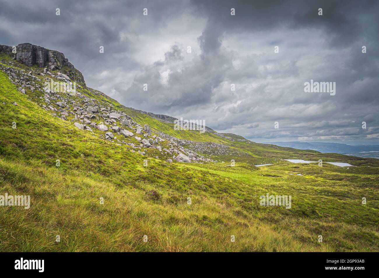 Green, long grass, large boulders and rubble on Cuilcagh Mountain mountainside with small lakes in valley below, Northern Ireland Stock Photo