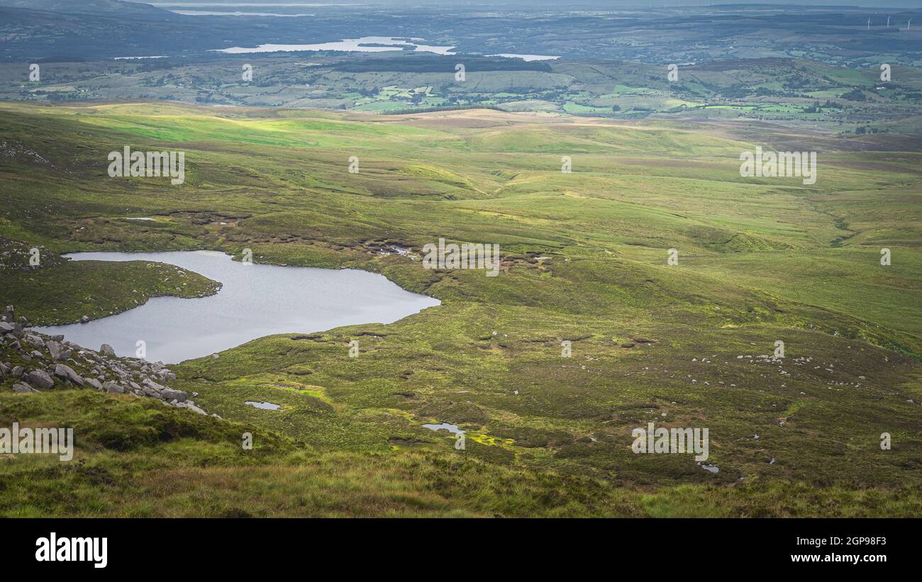 View from Cuilcagh Mountain on lakes, green meadows and fields with patches of sunlight in the valley below, Northern Ireland Stock Photo