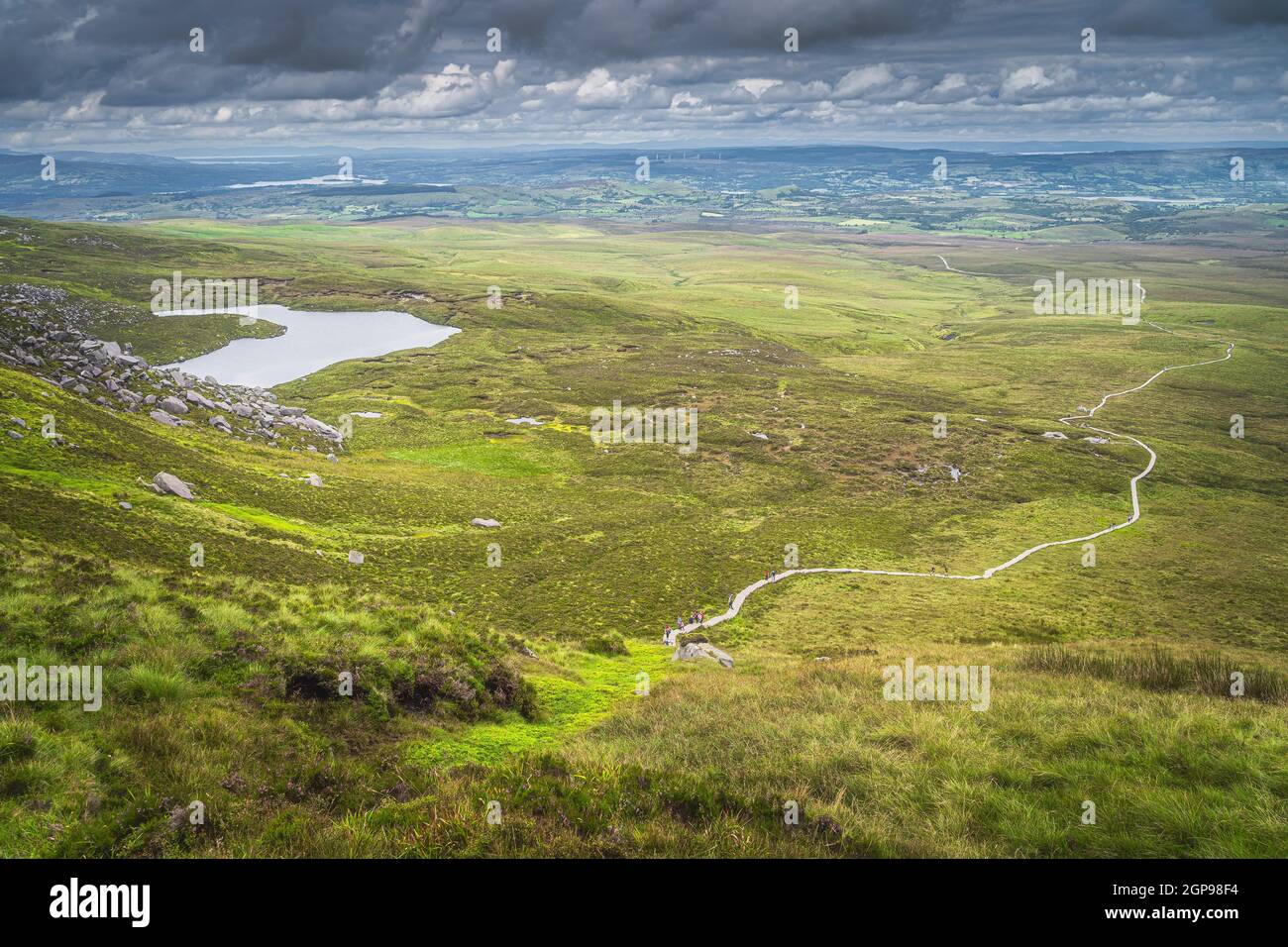 View from the mountain peak on winding wooden path of Cuilcagh Park boardwalk in the valley below with small lake, Northern Ireland Stock Photo