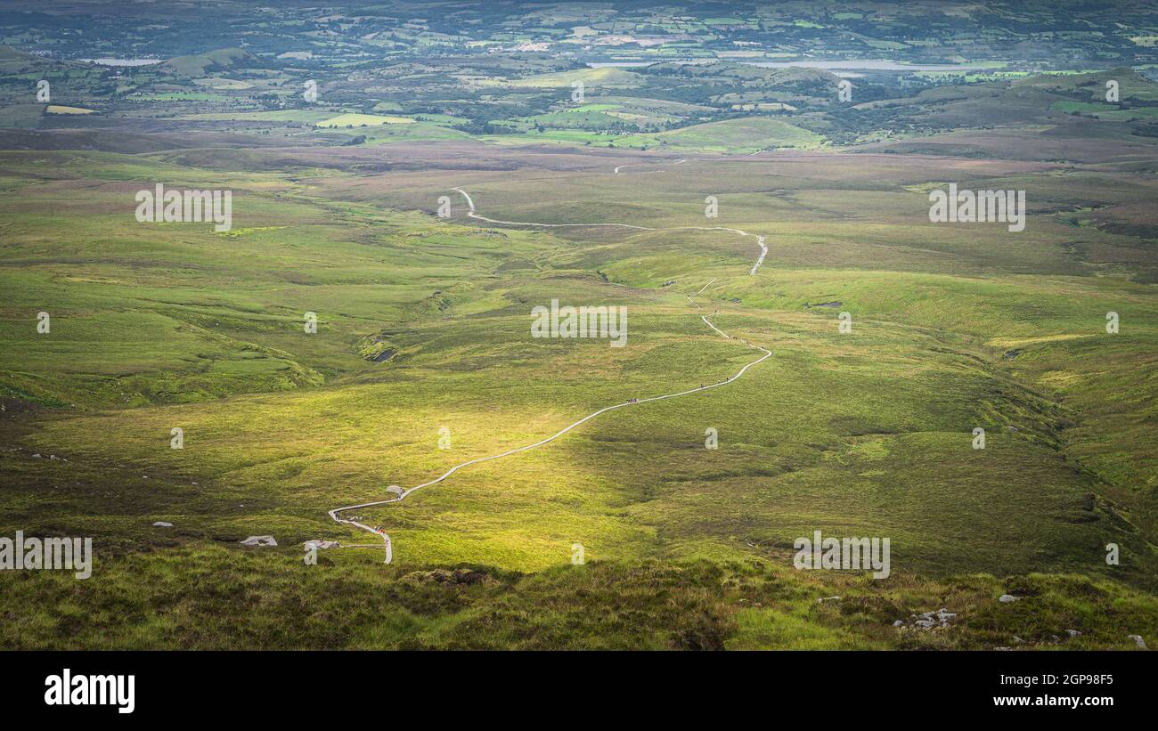 View from the mountain peak on winding wooden path of Cuilcagh Park boardwalk illuminated by sunlight in the valley below, Northern Ireland Stock Photo