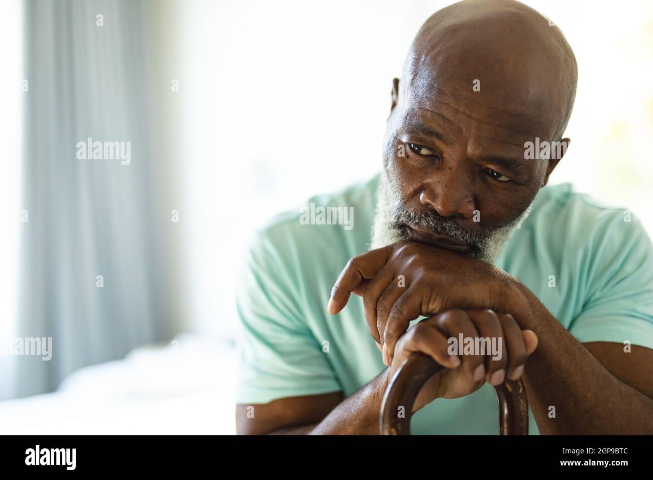 Thoughtful senior african american man in bedroom holding walking cane Stock Photo