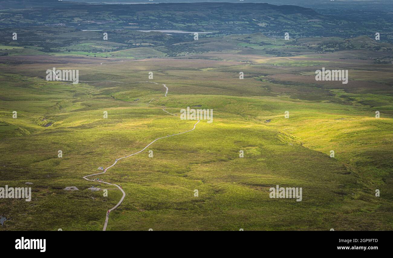 Drone or aerial view on winding wooden path and boardwalk between green fields illuminated by sunlight in Cuilcagh Mountain Park, Northern Ireland Stock Photo