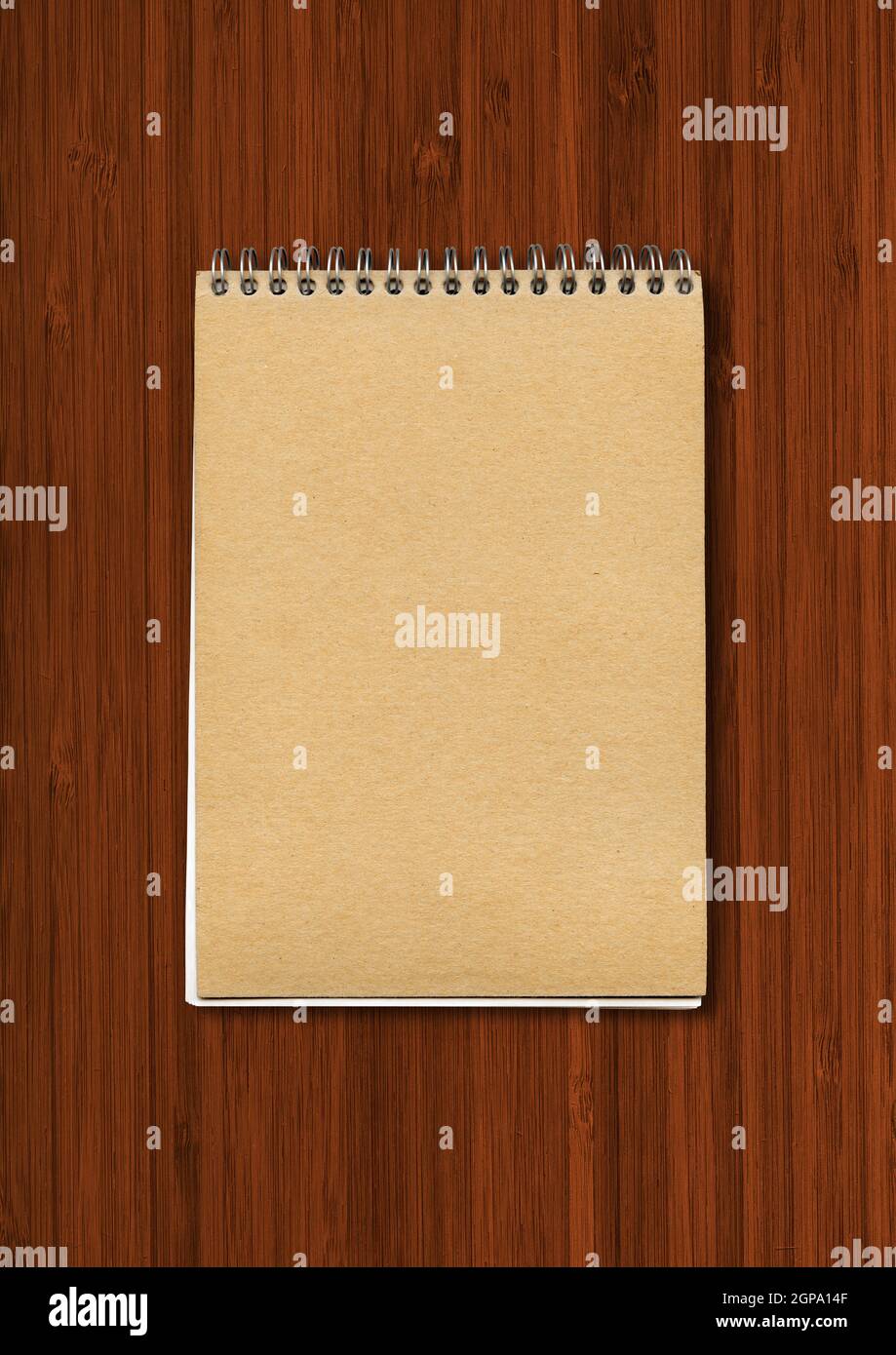 Spiral closed notebook mockup, brown paper cover, isolated on dark wood