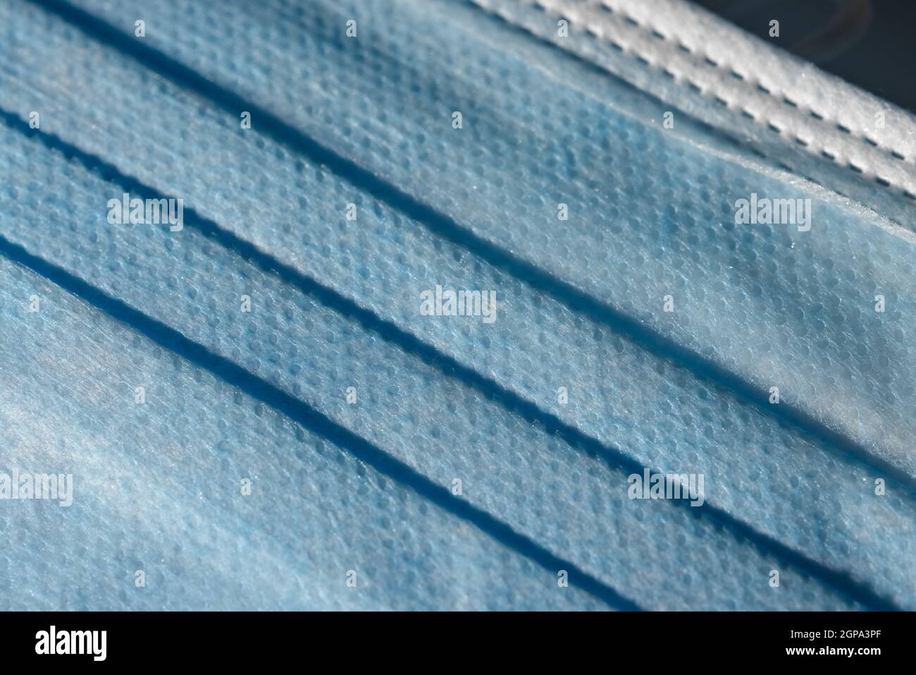 Blue dimpled texture and folds of a disposable 3-ply medical face mask. Mandatory use for many people in public spaces due to Covid aka coronavirus. Stock Photo
