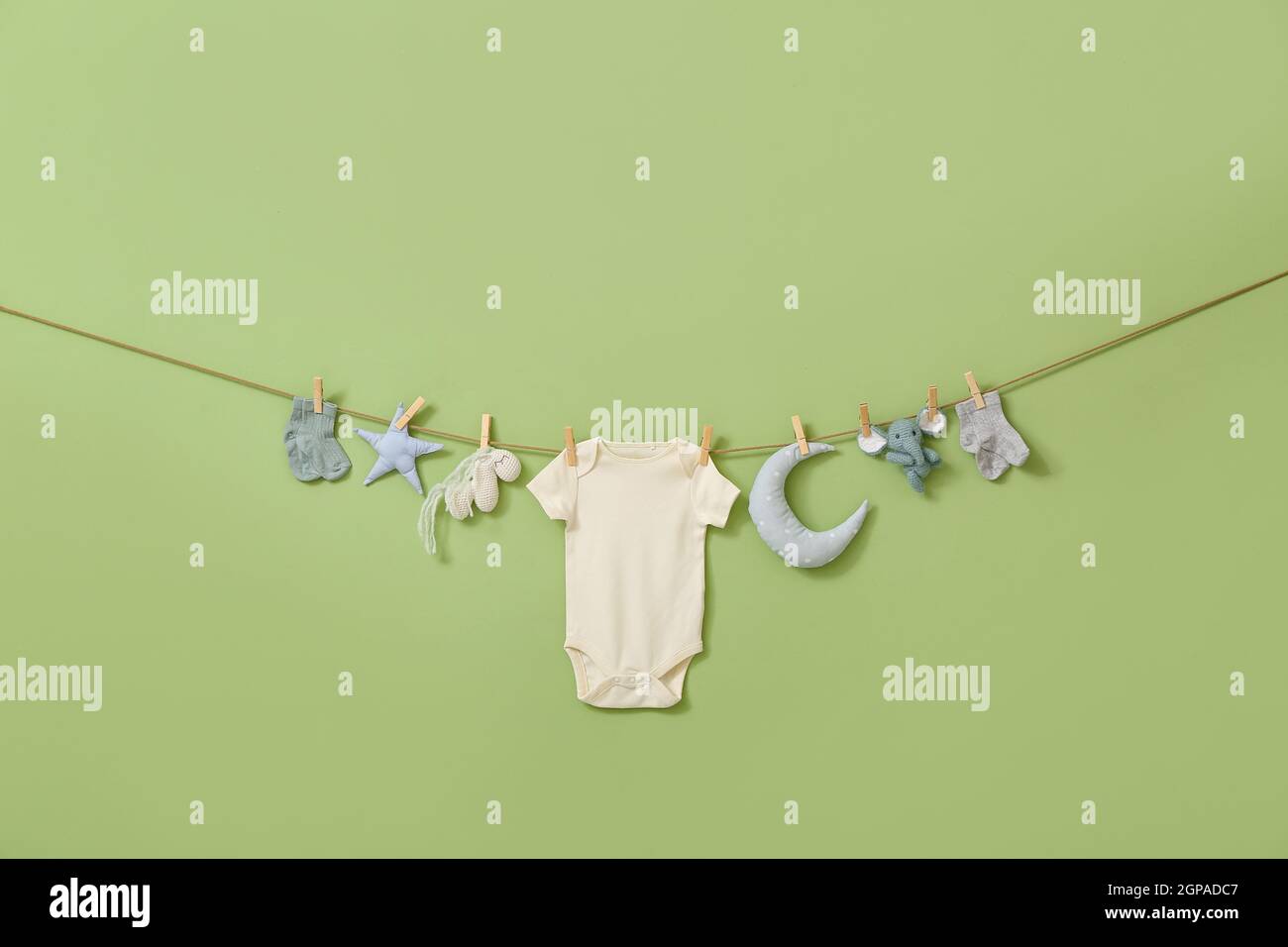 Stylish baby clothes and toys hanging on rope against green background ...