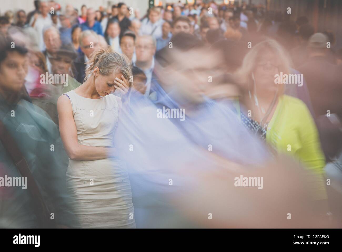 Crowd of people walking on city street - motion blurred image with unrecognizable faces - Young woman standing still, feeling down, depressed Stock Photo