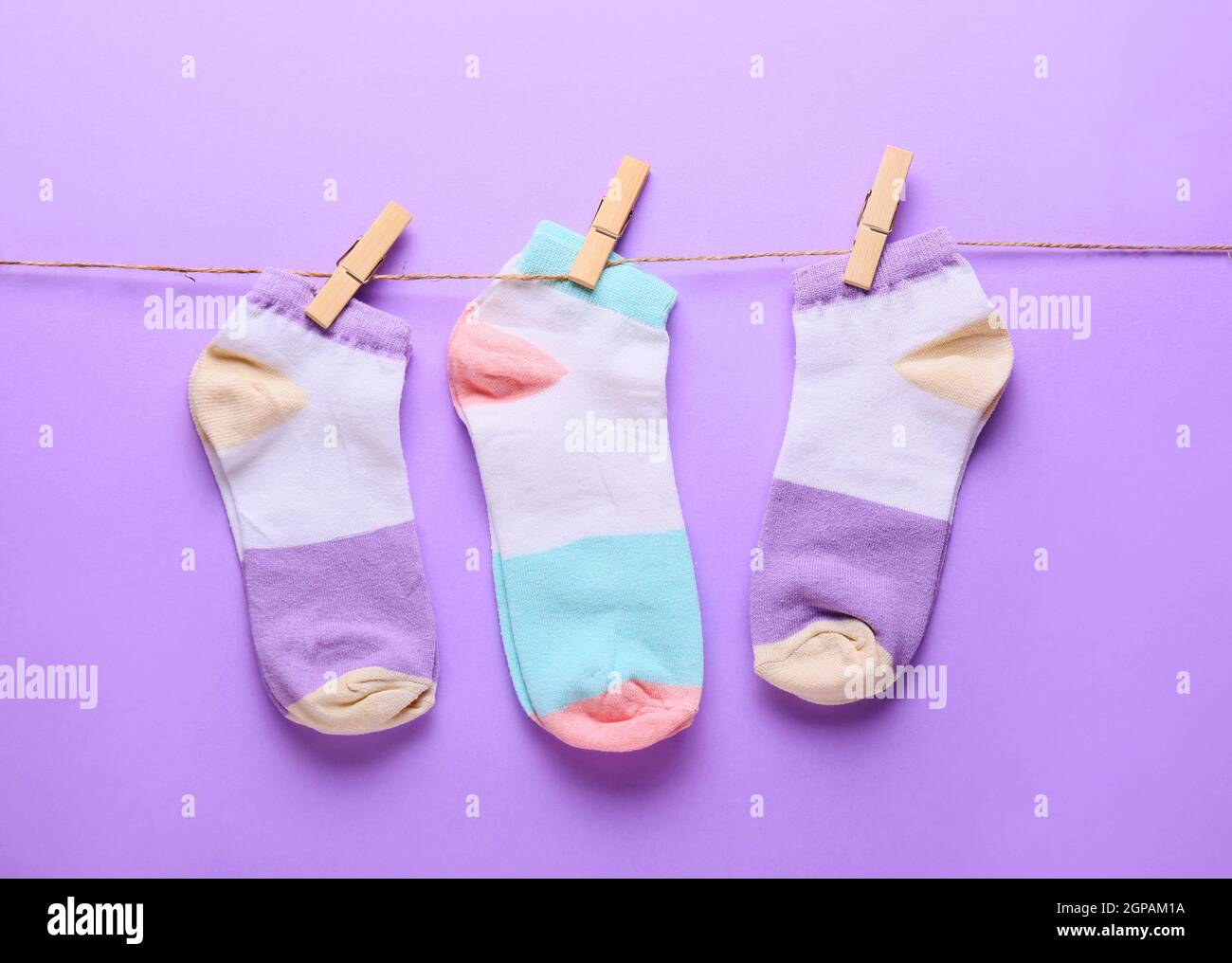 Different socks hanging on rope against lilac background Stock Photo ...