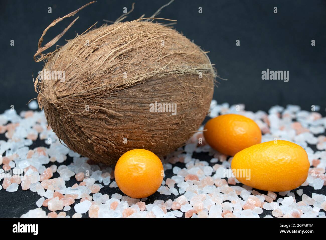 Coconut and kumquat with pink sea salt on black background. Stock Photo