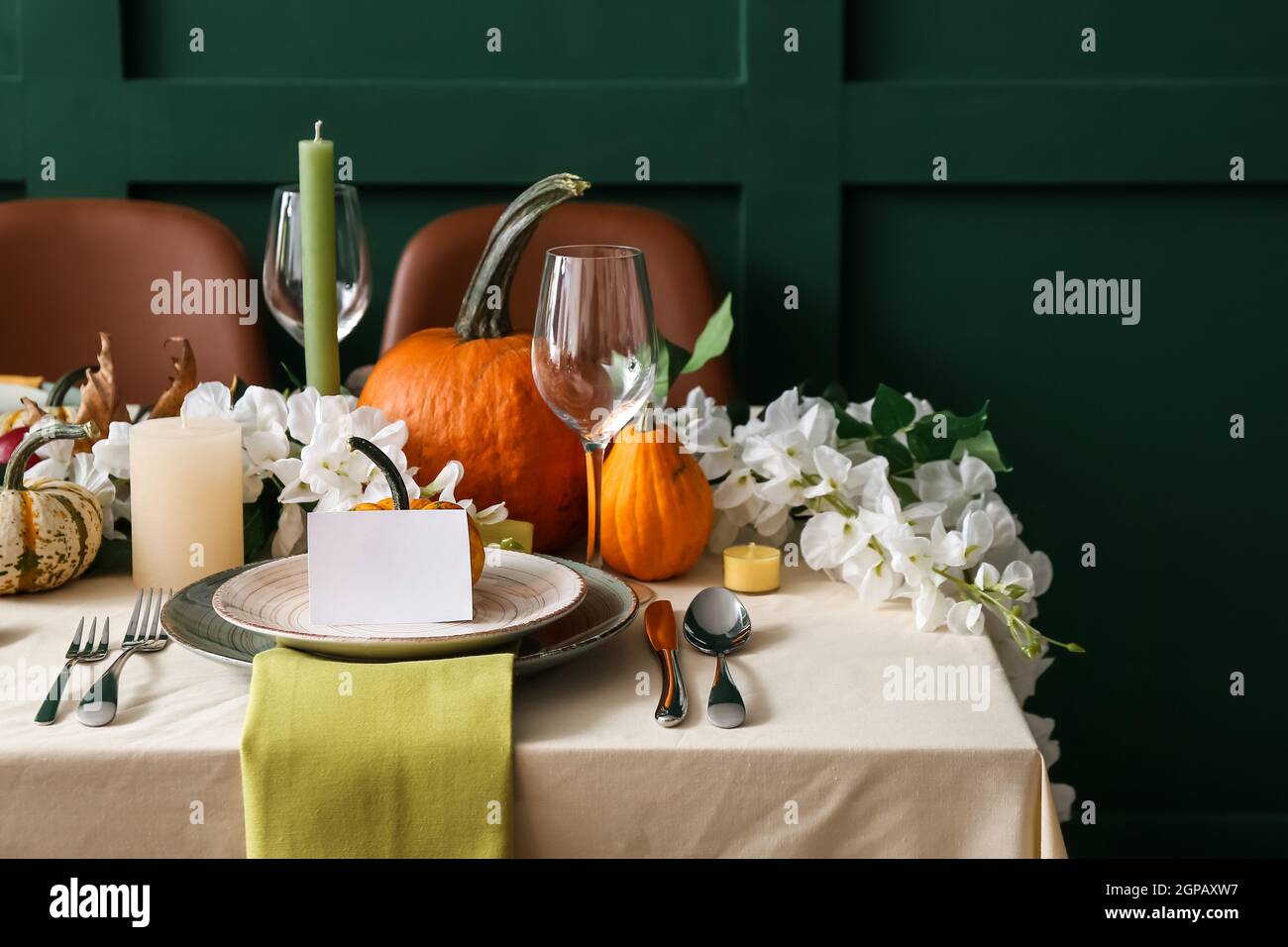 Autumn table setting with fresh pumpkins and flowers near green wall ...