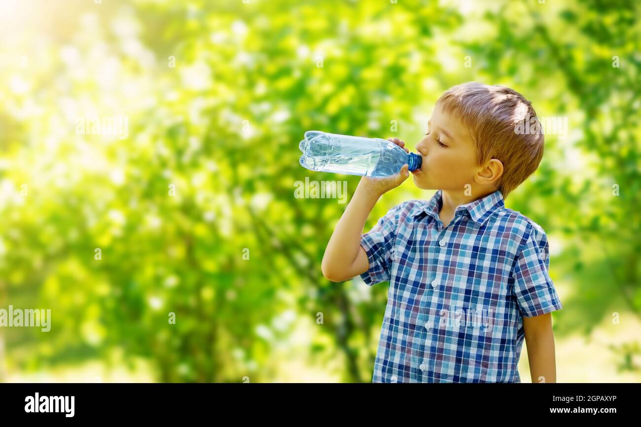 Cute boy drinking a bottle of pure water in nature. Concept of the provision of clean, mineral