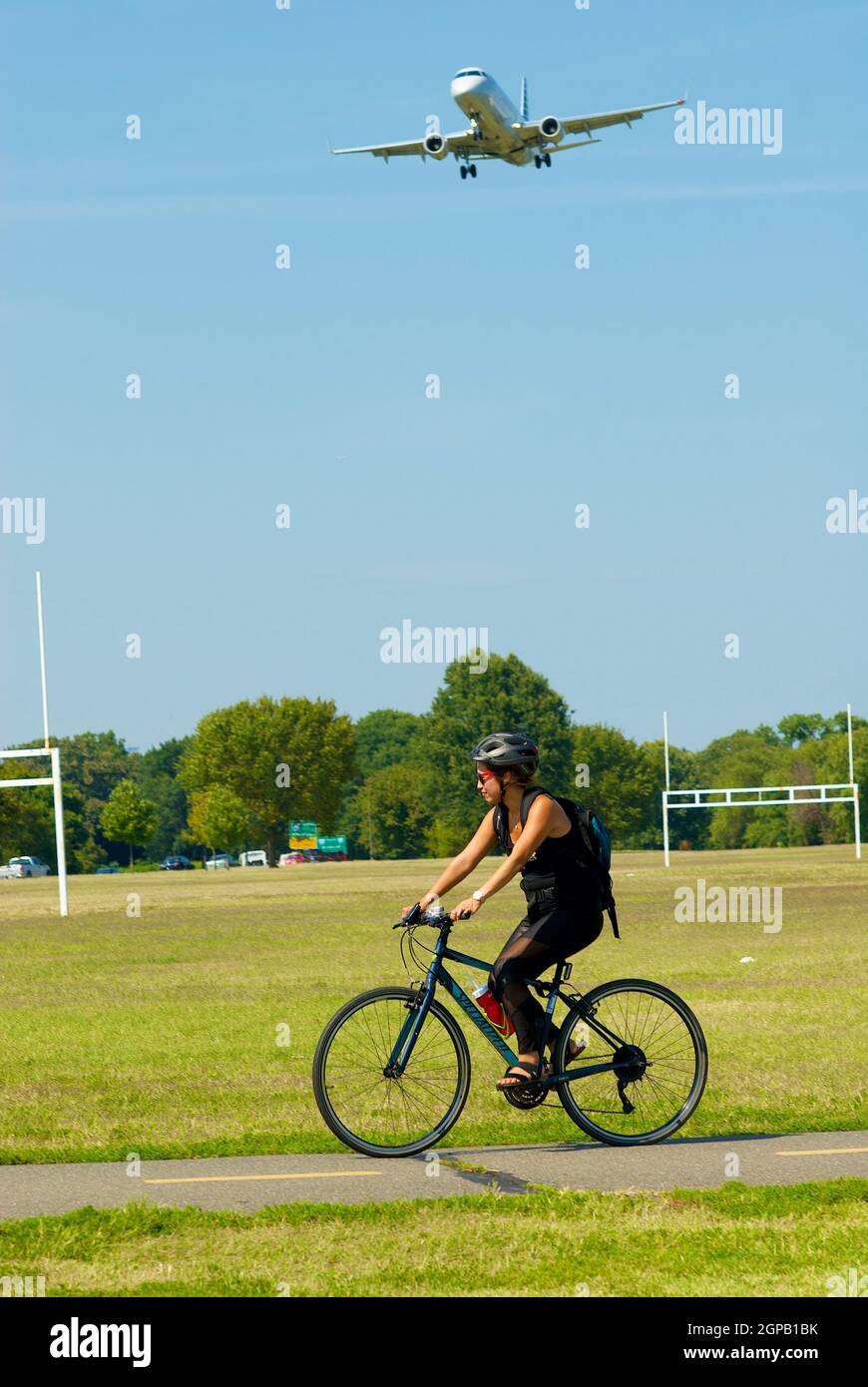 Arlington, Virginia, USA - September 11, 2019: A woman bikes at Gravelly Point as a regional jet approaches Ronald Reagan Washington National Airport. Stock Photo