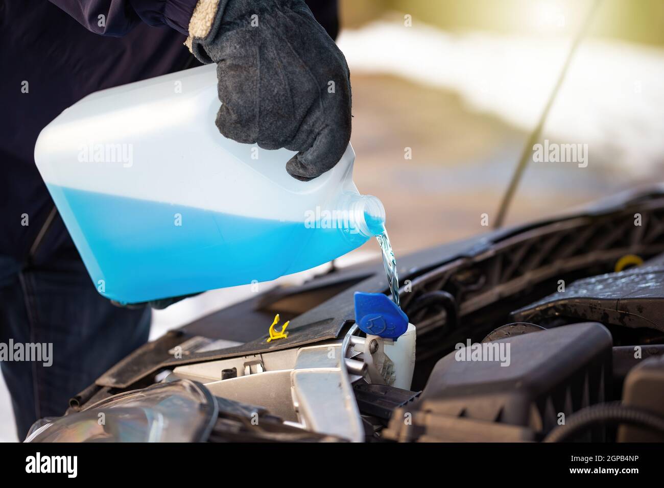 Man filling antifreeze coolant for cleaning front window with snow in