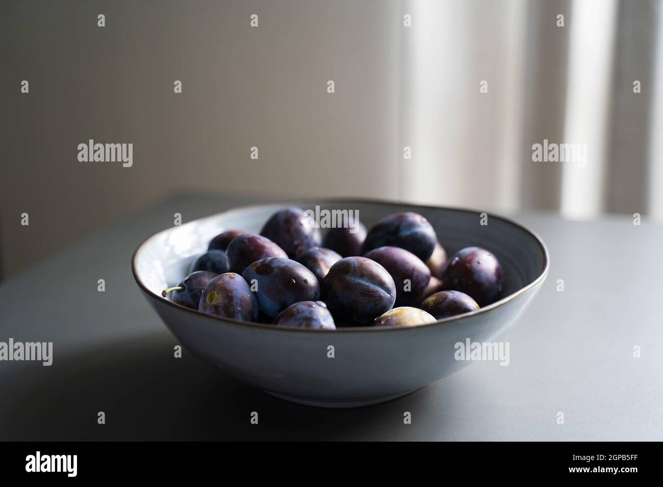 perspective view of fresh ripe plum fruits in vintage elegant grey bowl ...