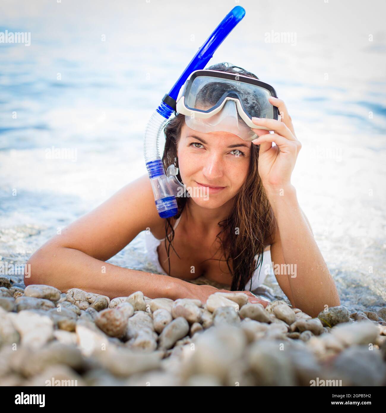Pretty, young woman on a beach during her summer vacation with snorkel lying on beach with snorkeling mask and fins smiling happy enjoying the sun on Stock Photo