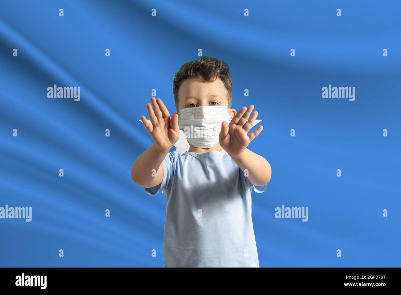 Little white boy in a protective mask on the background of the flag of Somalia. Makes a stop sign with his hands, stay at home Somalia. Stock Photo