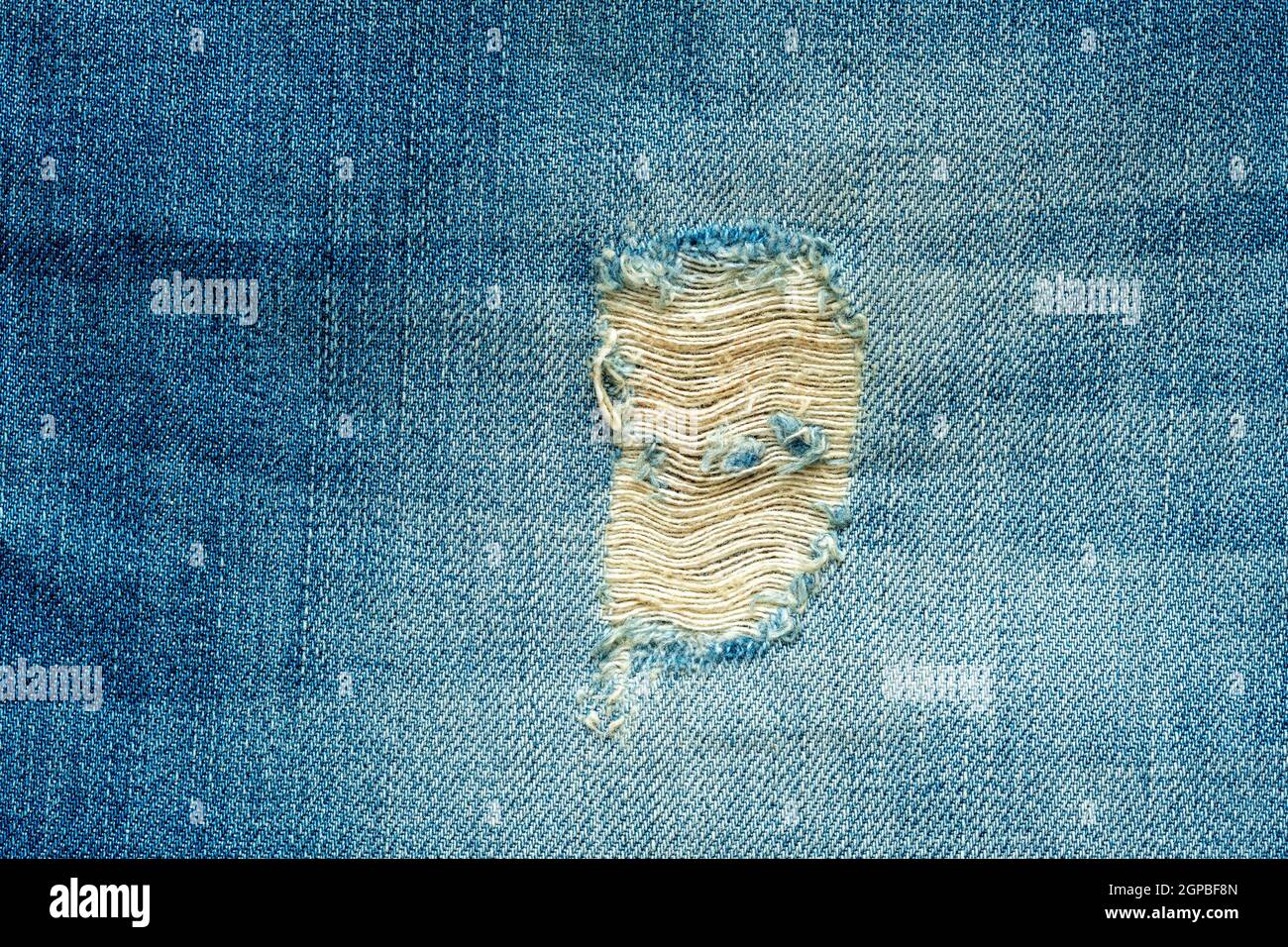 Hole and threads on denim jeans. Ripped blue jeans background. Close up