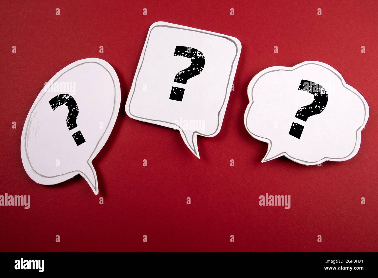 Three speech bubbles with question marks on a red background. Stock Photo