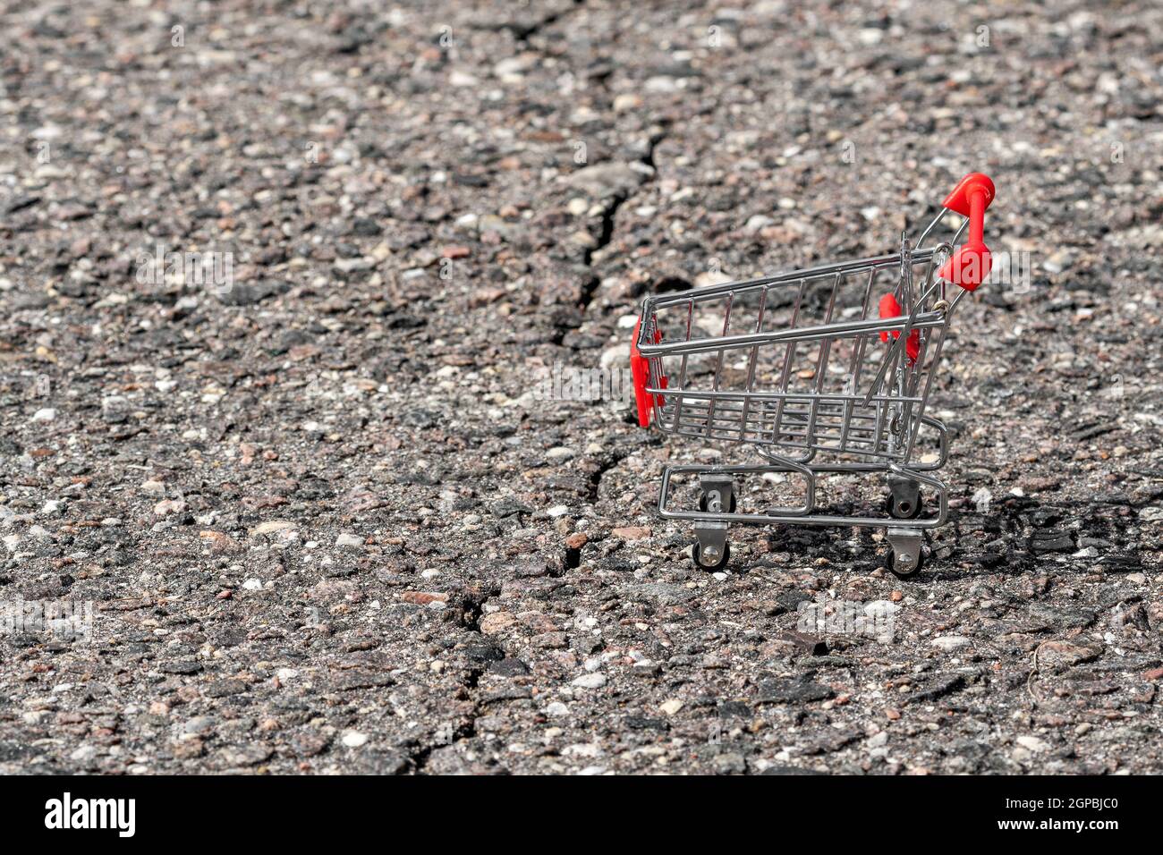 Empty shopping cart beside the asphalt crack. Concept of problems in