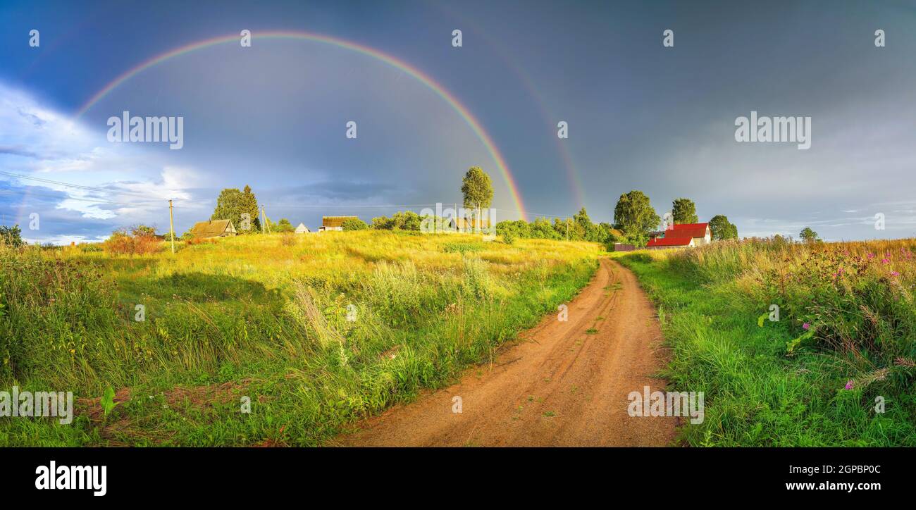 Rainbow over stormy sky. Rural landscape with rainbow over dark stormy sky in a countryside at summer evening. Stock Photo