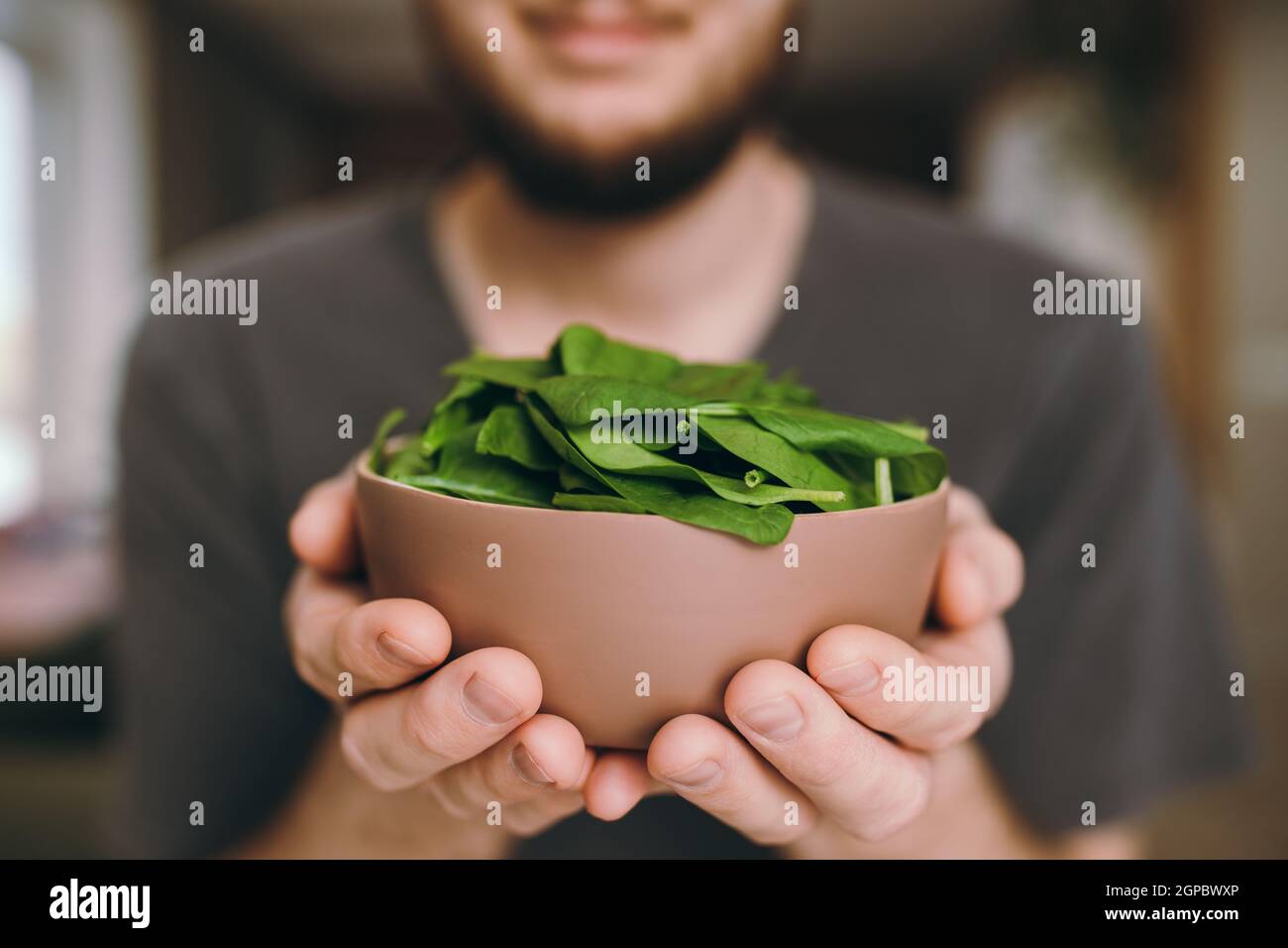 Hands of smiling man holding fresh green salad leaves of spinach on blurred background. Healthy vegetarian eating concept. Green leaves of spinach. Gi Stock Photo