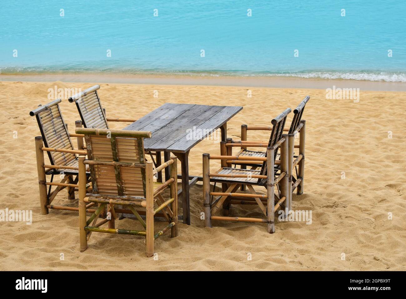 Wooden bamboo furniture, table and five chairs around on sand beach