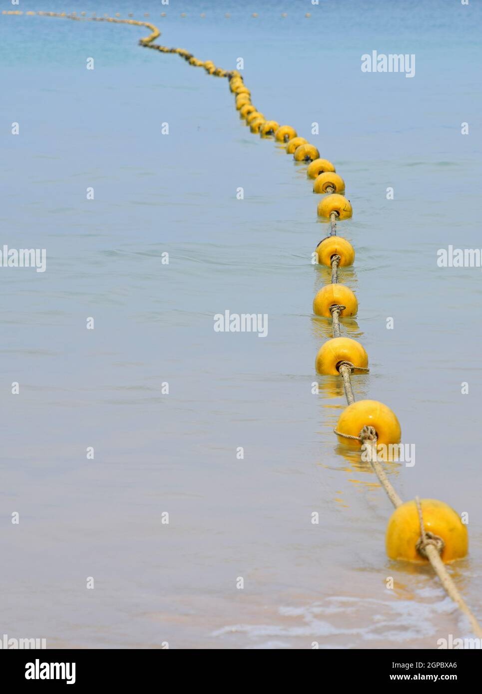 Chain of yellow polystyrene sea marker buoys with cable tow in blue sea water, in perspective Stock Photo