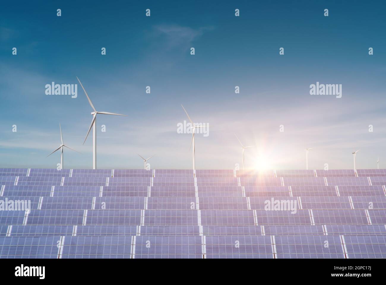 Solar panels with wind turbines against blue sky background. Concept of renewable green energy is friendly. Stock Photo