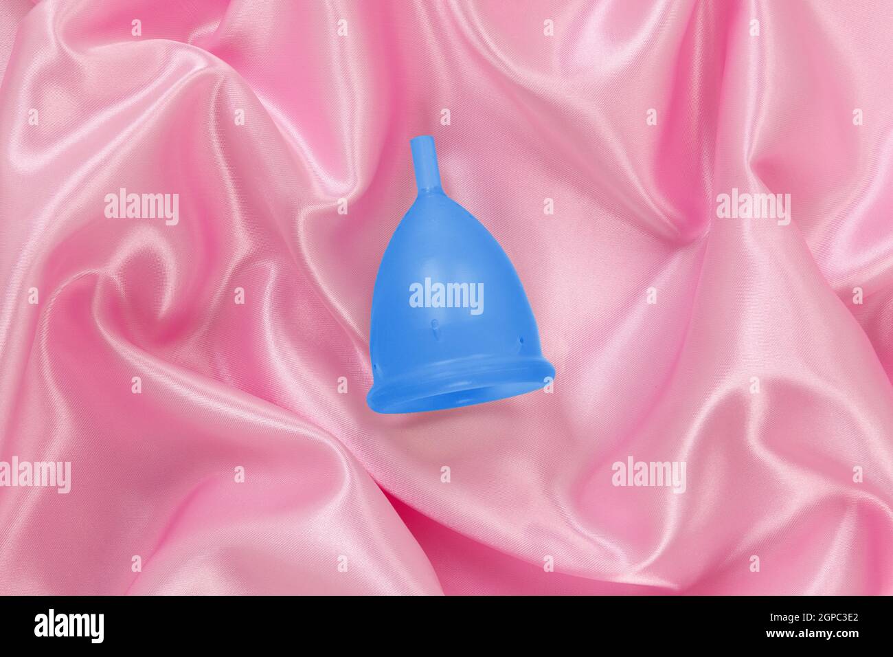 Menstrual cup on pink satin background. Feminine hygiene. Stock Photo