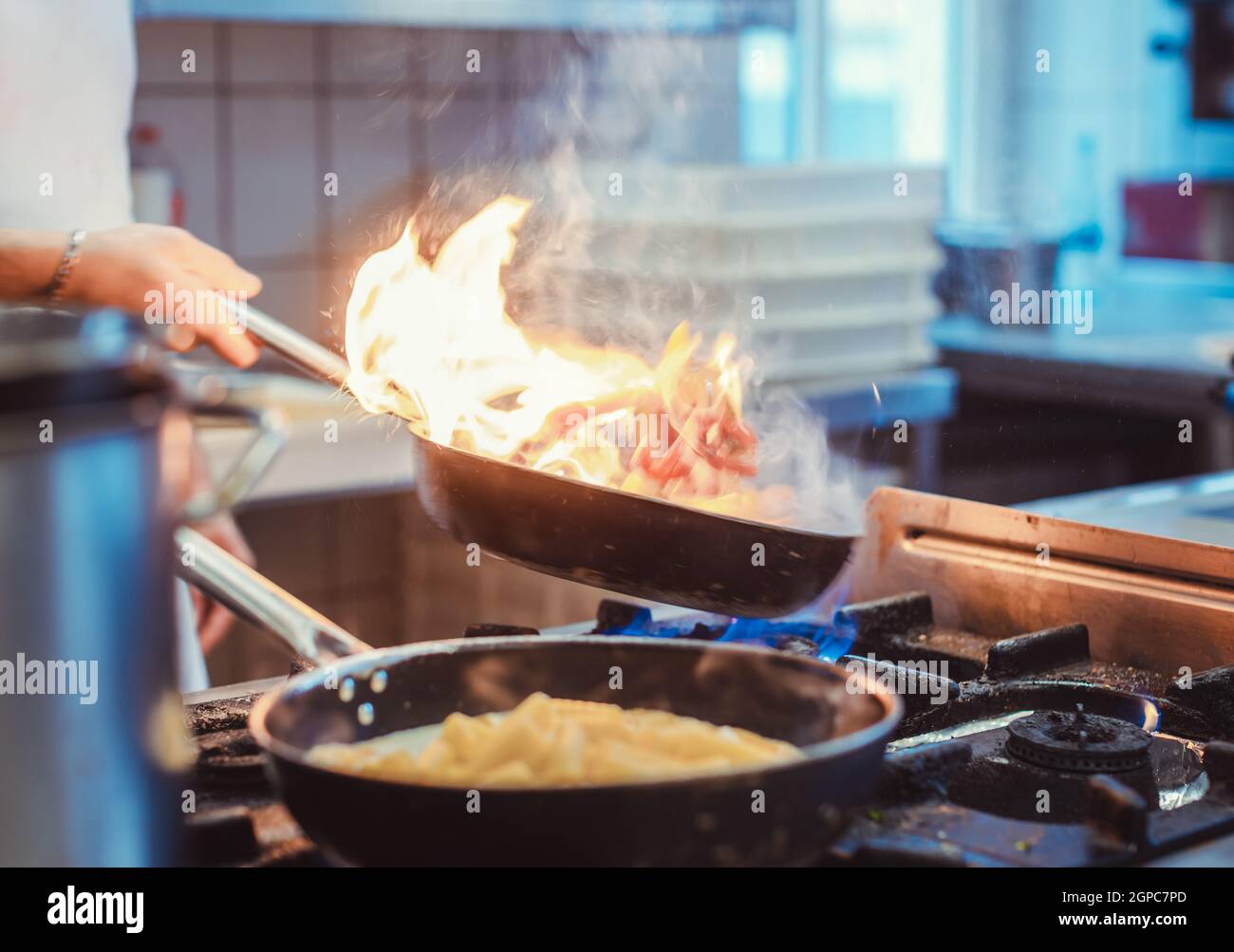 Chef cooking in a restaurant kitchen with flames of fire on his pan Stock Photo