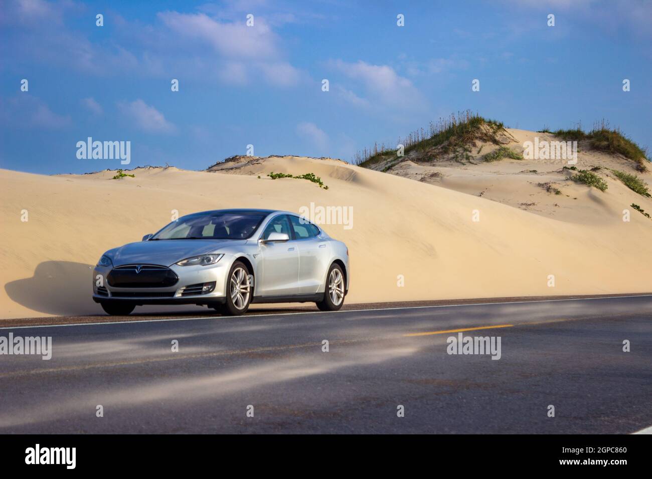 A sliver 2014 Tesla Model S next to the shifting sand dunes of South Padre Island, Texas along Ocean Boulevard. Stock Photo