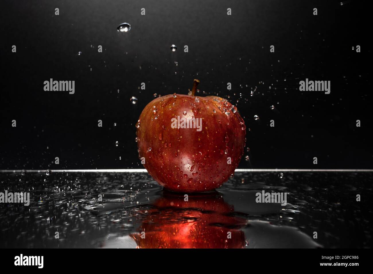 A red apple resting on a mirror with falling water drops Stock Photo