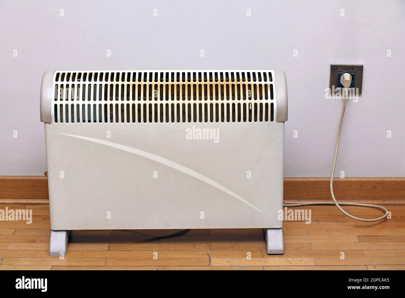 Electric heater on wooden floor and plugged into socket on a wall inside  interior Stock Photo - Alamy