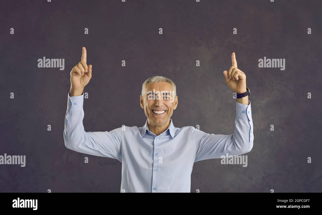 Joyful senior man pointing index fingers at copy spase over head offering something to choose from. Stock Photo