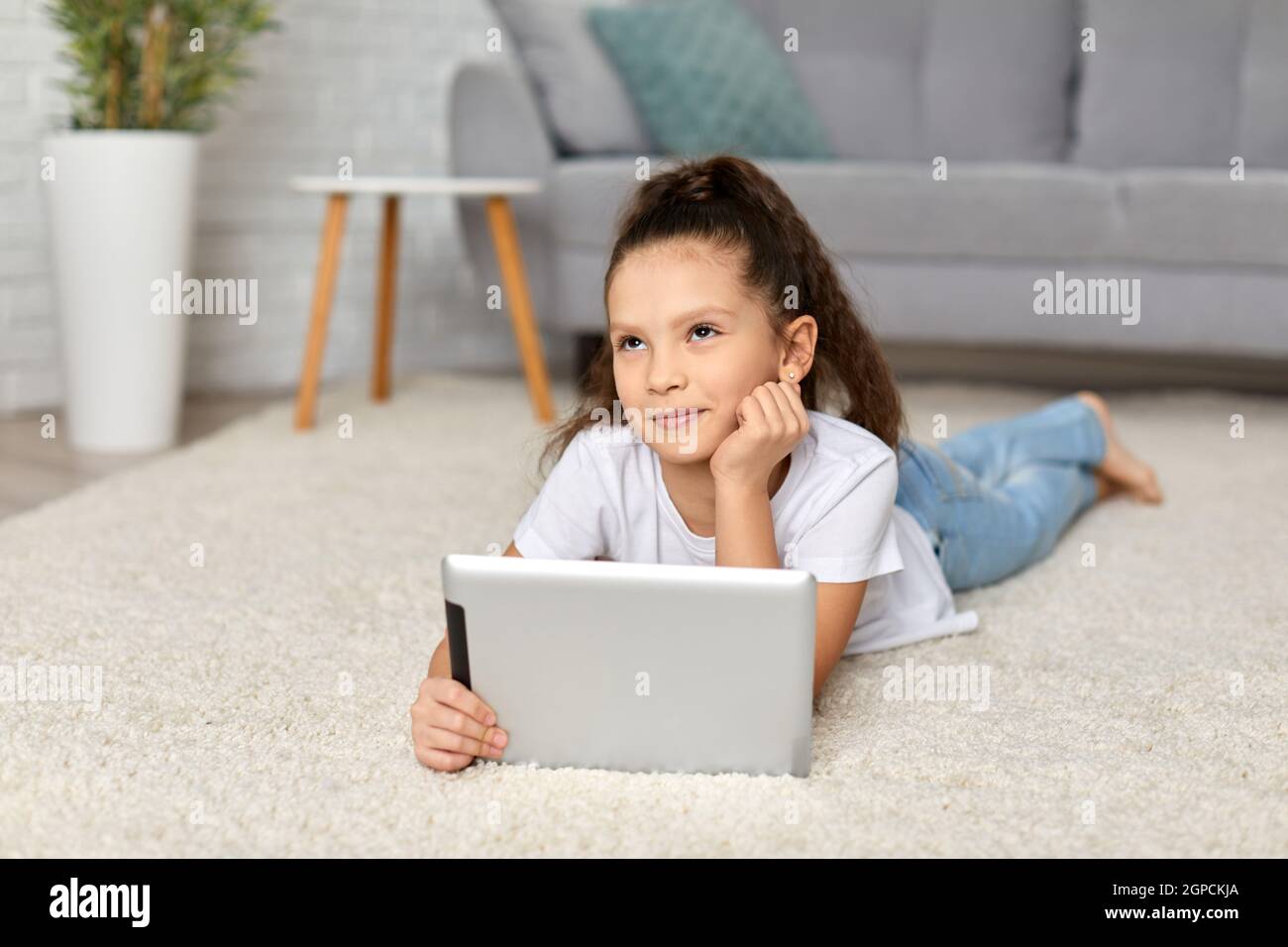 cute happy little child girl lying on the carpet and using digital ...
