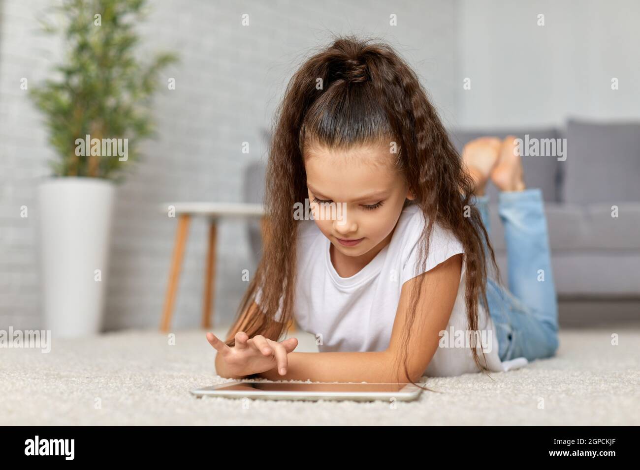 cute happy little child girl lying on the carpet and using digital ...