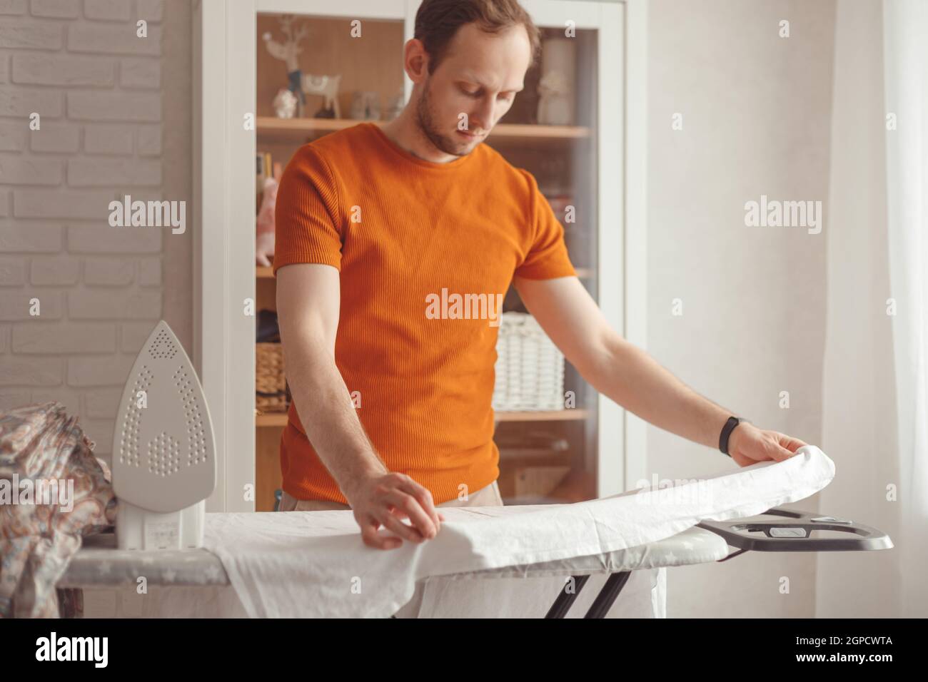 Young caucasian man ironing children's sheet on ironing board at home. Men doing home chores Stock Photo