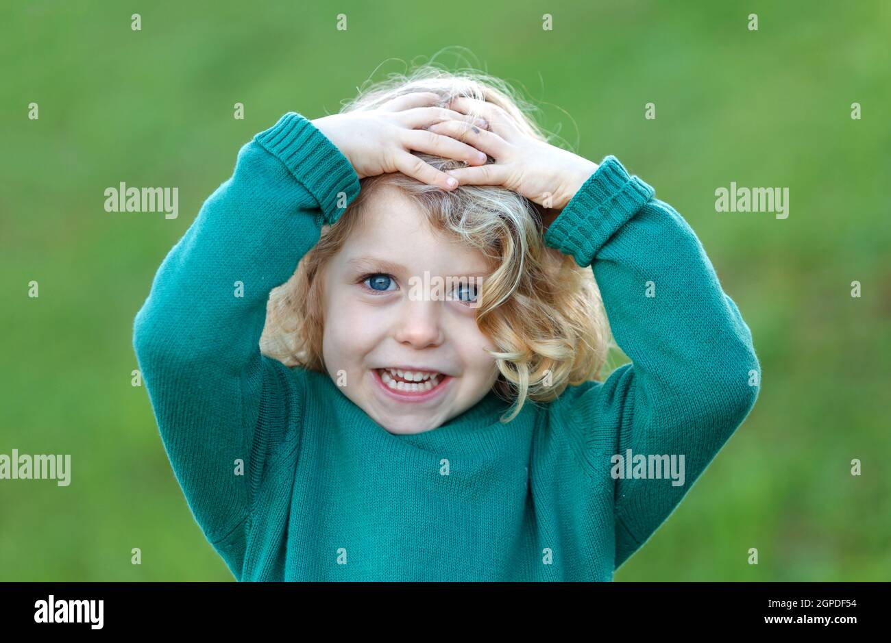 Happy blond child with his hands on the head in a park Stock Photo