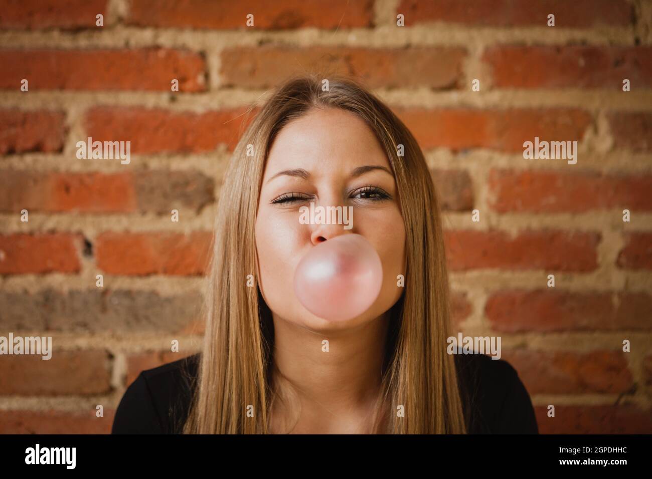 Funny girl making a pomp with a bubble gum and a brick wall of background Stock Photo