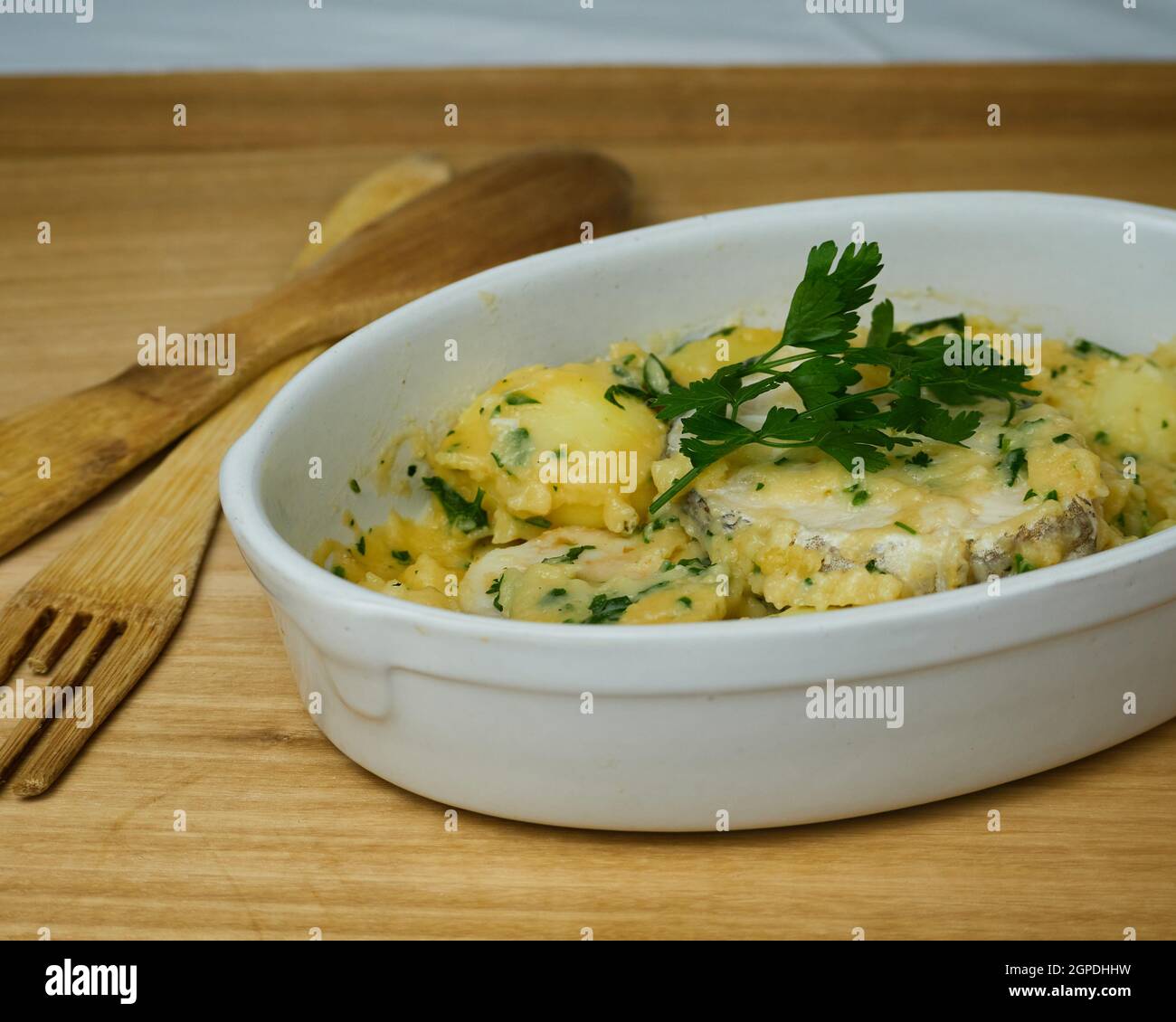 Hake on a green sauce with parsley leaves in a ceramic platter with wooden cutlery Stock Photo