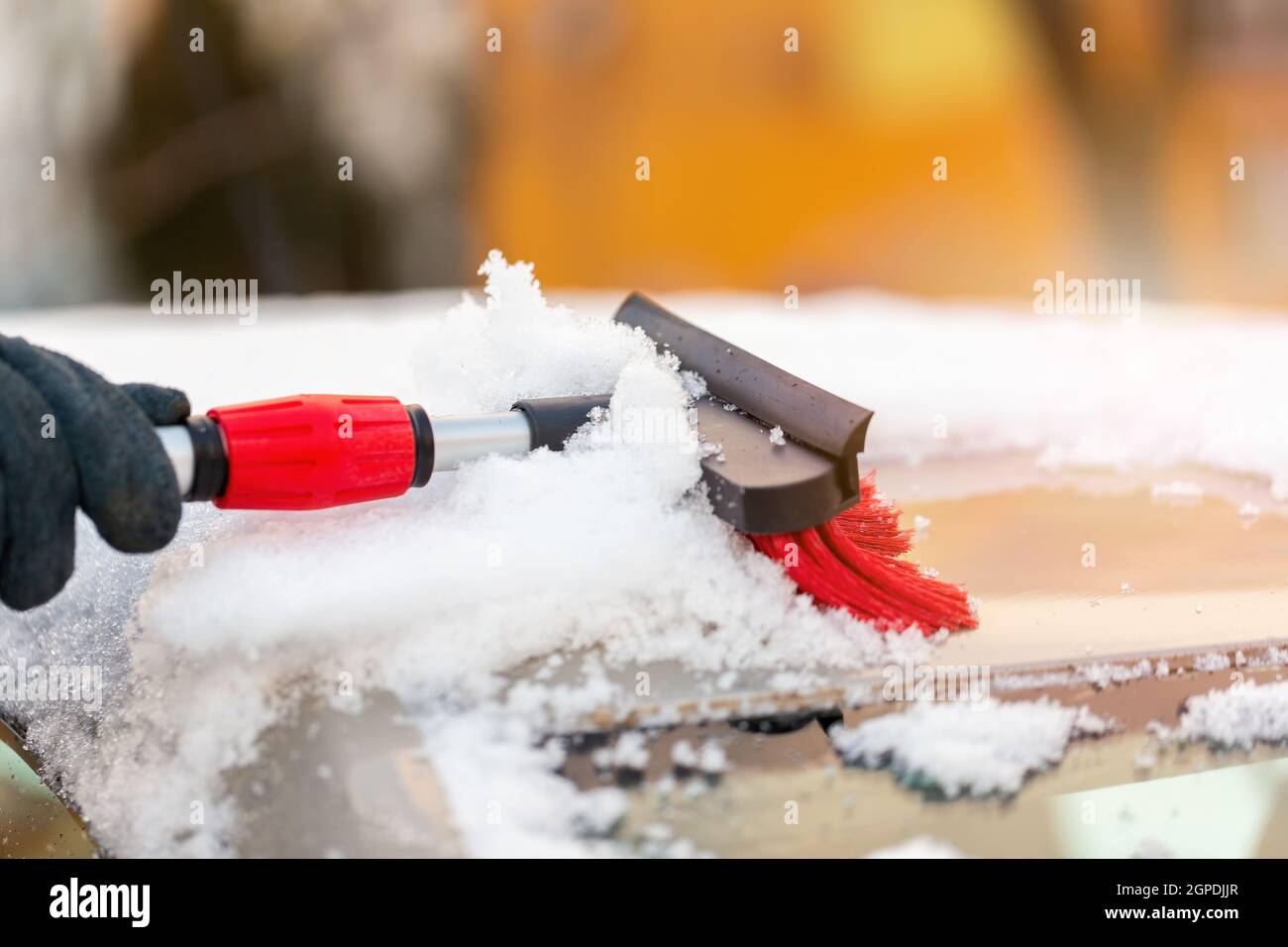 Human cleaning snowy cover from roof of the car in sunlight. Person sweeping snow from automobile with broom. Hand using a tool in winter. Stock Photo