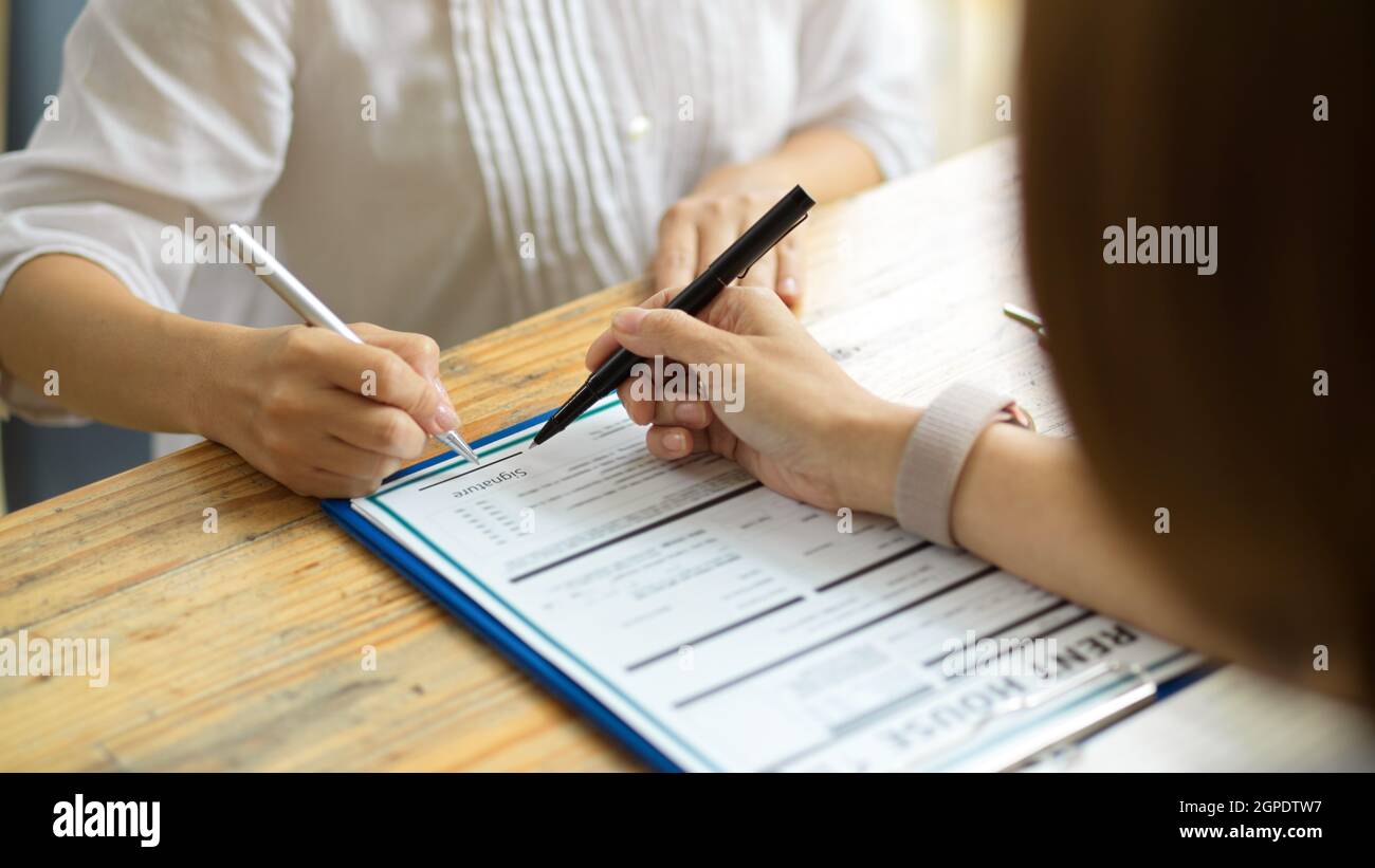 A new renter signing her signature on a home rental contract form in the presence of a real estate agent. realtor and client close the deal Stock Photo
