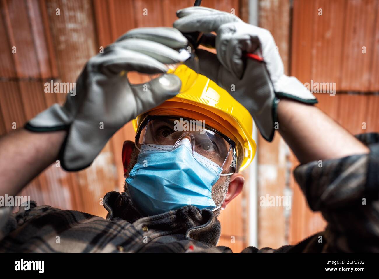 Electrician worker at work replaces the light bulb protected by helmet, safety goggles and gloves. Wear the surgical mask to prevent the spread of Cor Stock Photo
