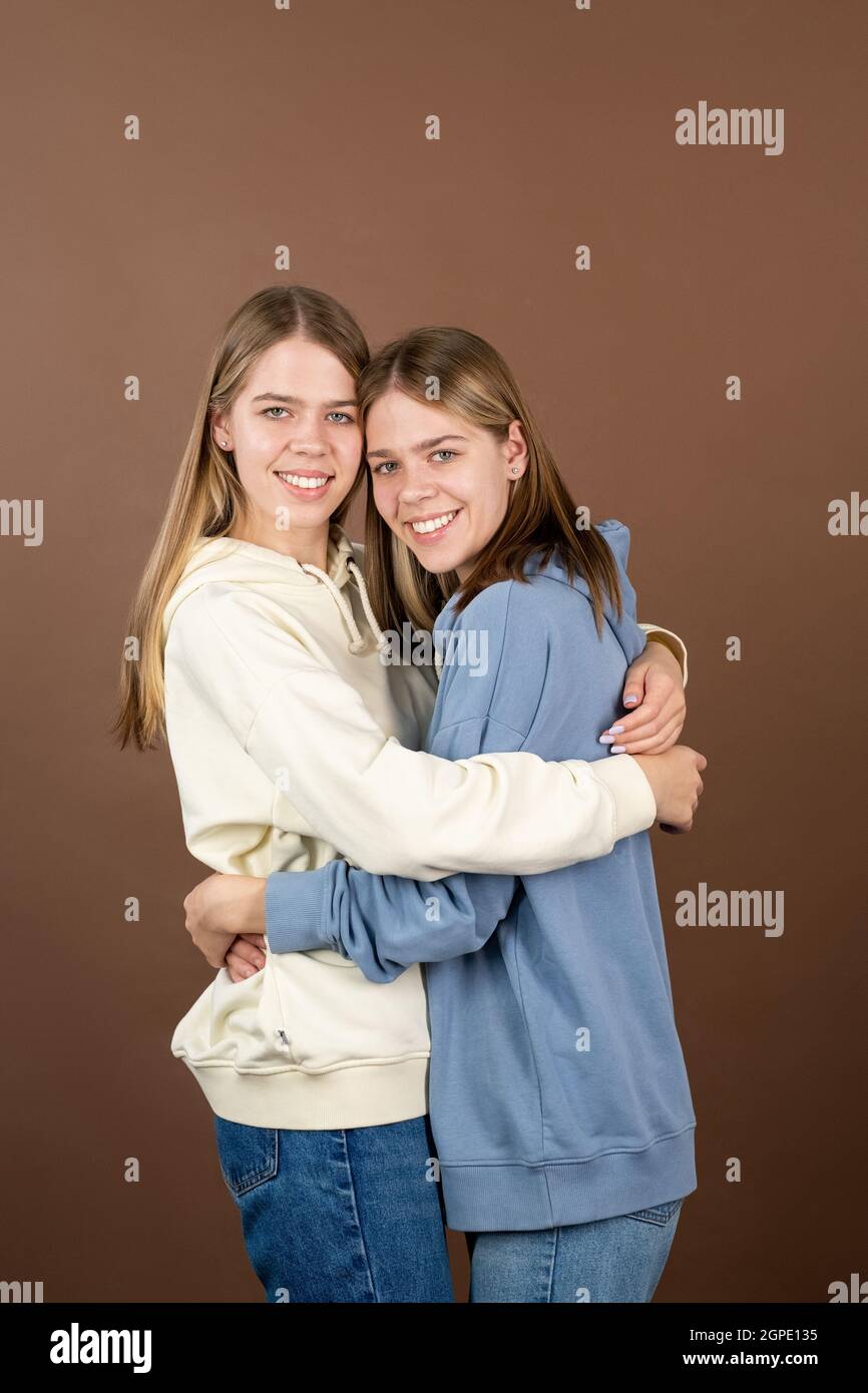 Cheerful twin girls in sweatshirts standing in embrace in front of camera Stock Photo