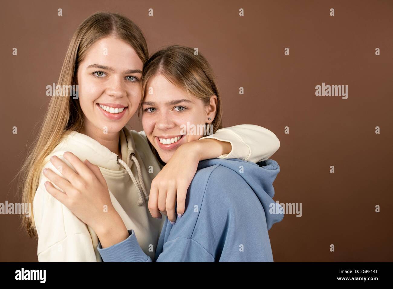 Two joyful teenage girls standing in embrace and looking at you with toothy smiles Stock Photo