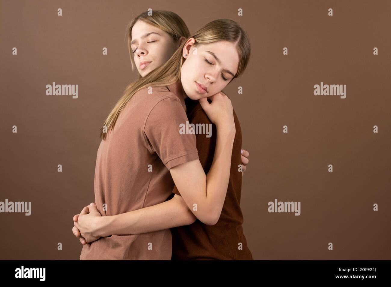 Affectionate twin girls in shirts standing in embrace in front of camera Stock Photo