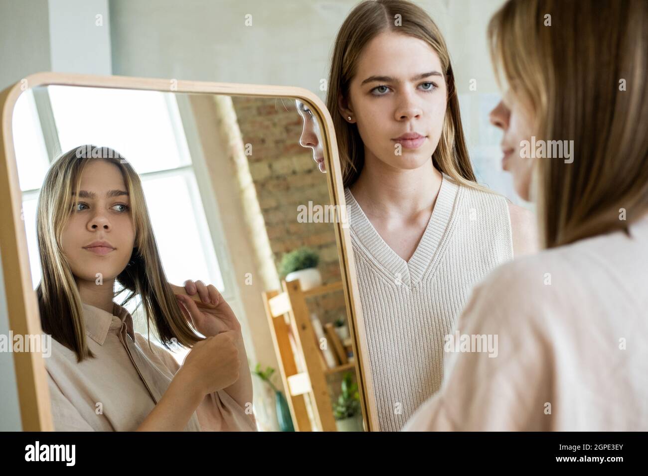 Serious teenage girl looking at her twin sister brushing hair in front of mirror Stock Photo