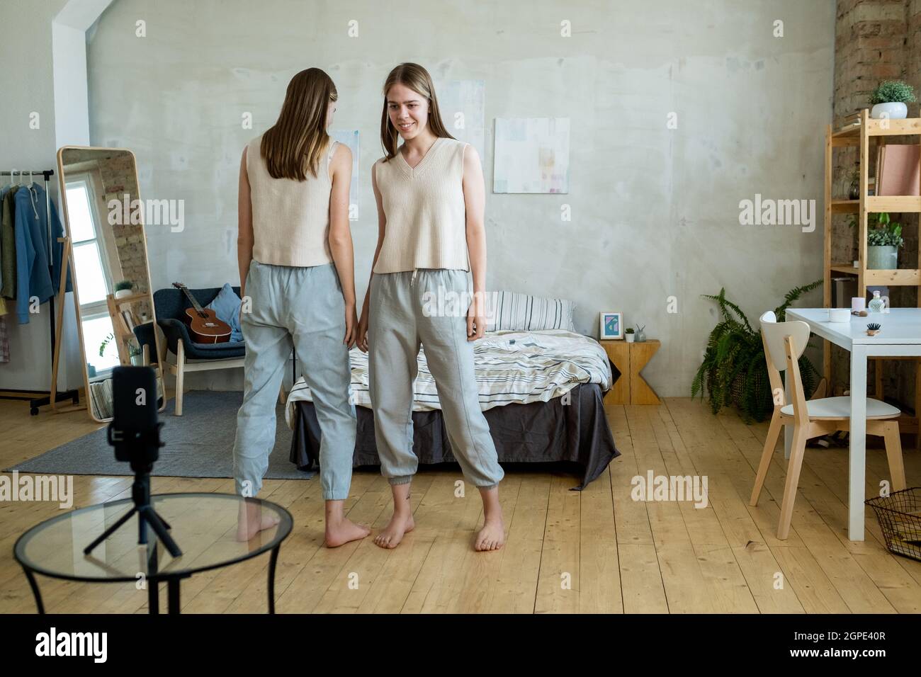 Two cute teenage girls standing in front of smartphone camera during livestream in bedroom Stock Photo
