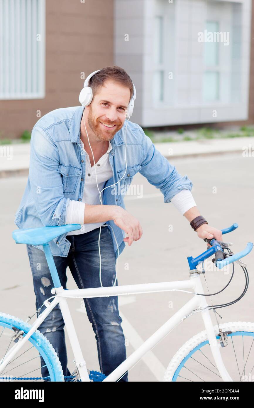 Casual guy next to a vintage bicycle listening music with headphones wearing denim shirt Stock Photo