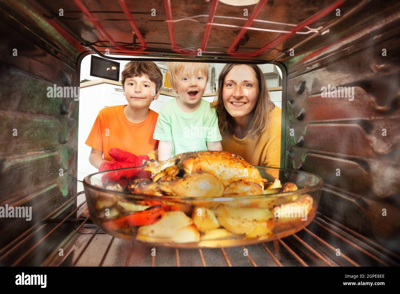 Mother and two boys take roasted chicken from oven Stock Photo