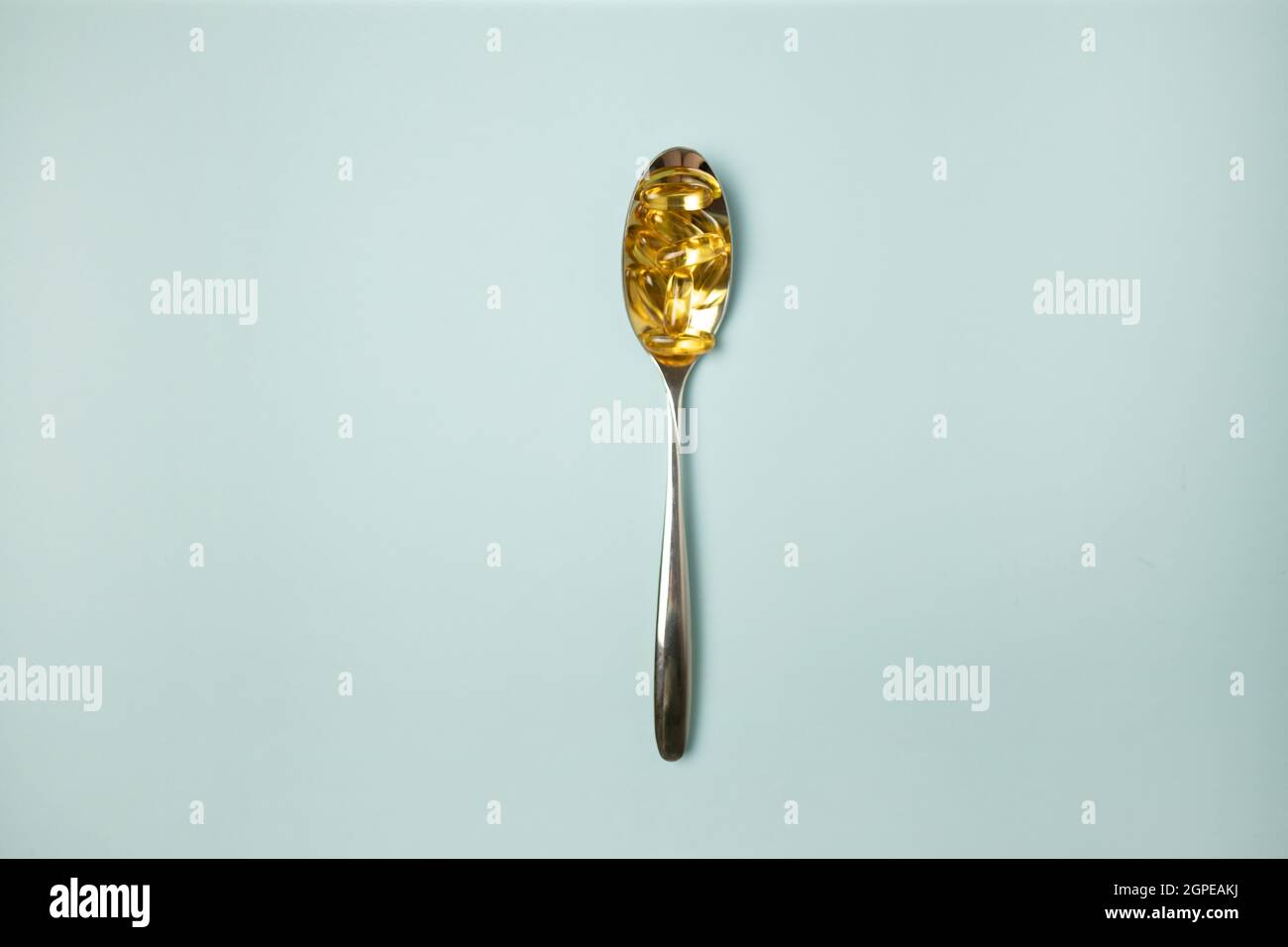 Metal spoon of Omega-3 capsules on blue background with copyspace Stock Photo